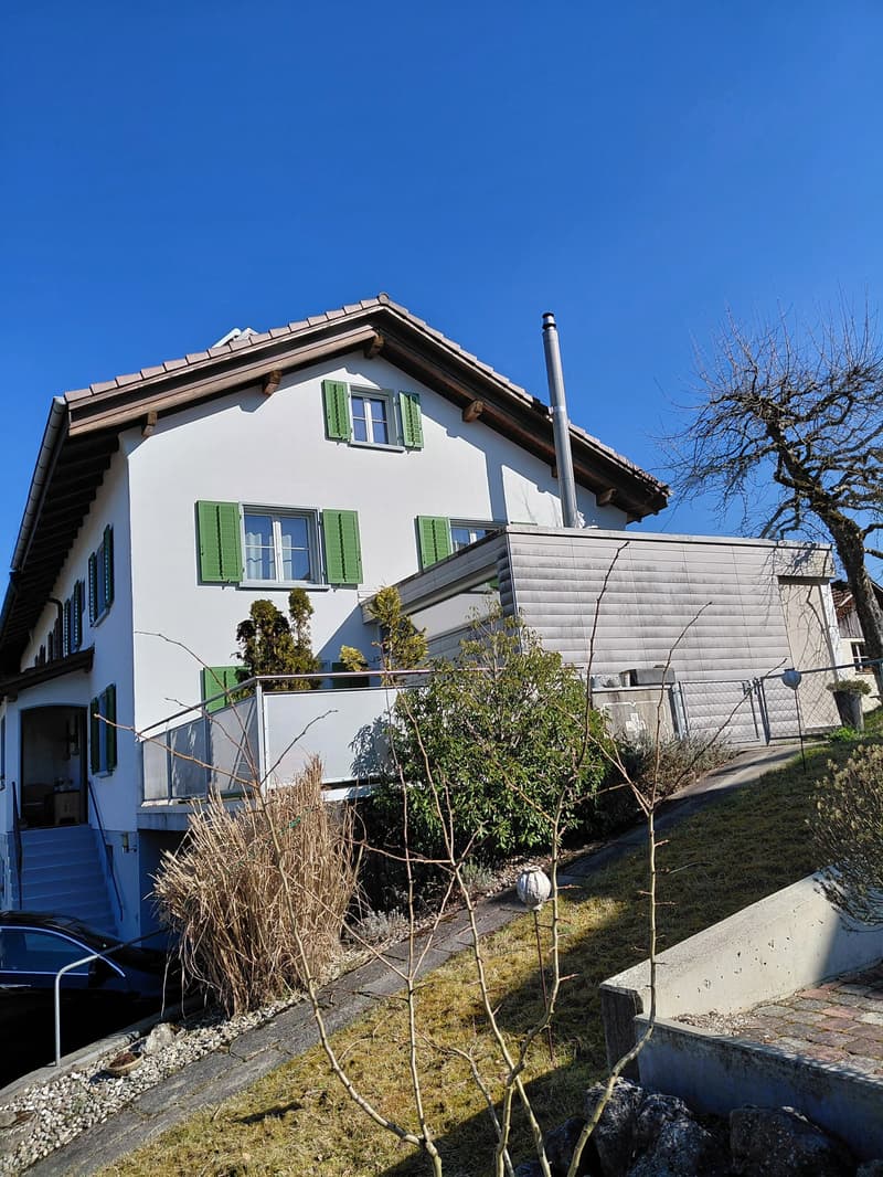 2 story house, white exterior, green shutters, raised ground floor, balcony, car parked nearby