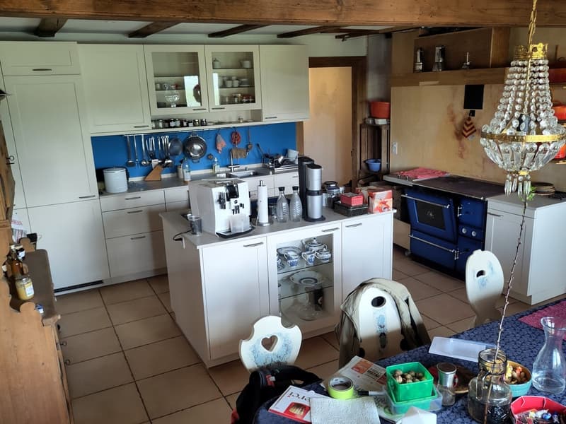 modern kitchen with white cabinets, blue backsplash, island with coffee machine, sink, and dishwasher, chandelier, dining table with chairs