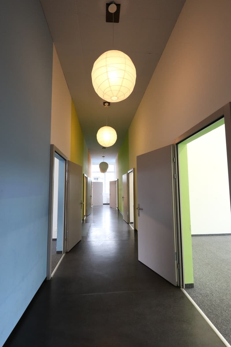 empty hallway, gray flooring, yellow, blue and green wall colors, ceiling-mounted hanging lights