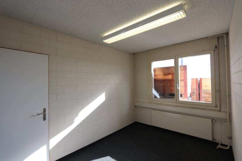 Empty room, white brick walls, white door, white ceiling, single window, single lamp, black carpet floor, white pipes