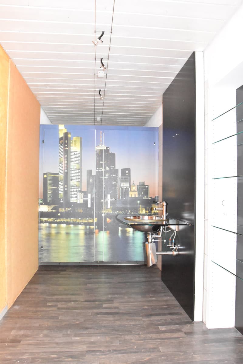 wooden floor, large wall-covering with city view, sink with metal faucet, glass wall with metal shelves, wall lighting