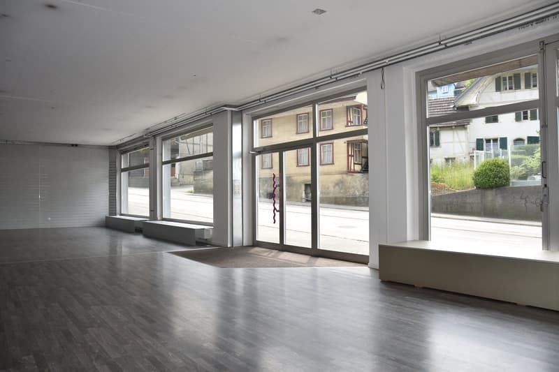 Empty room, hardwood floors, glass walls, wooden benches, large windows, view of the street