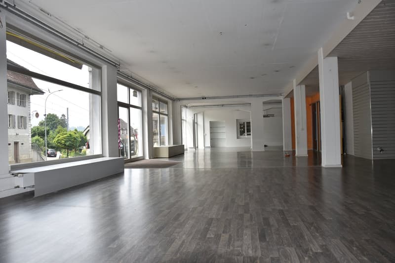 Large open space, hardwood floors, large windows, bench, and industrial-style interior design.