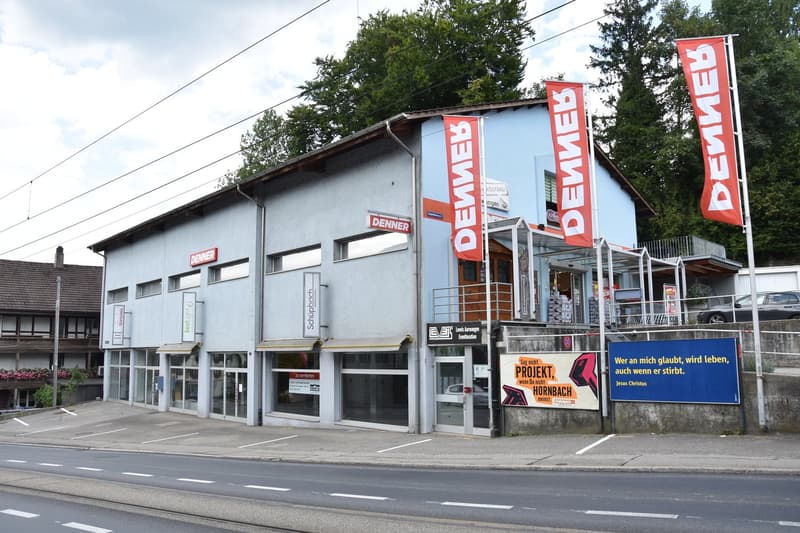 Commercial building with multiple storefronts, banners, and parked cars in front