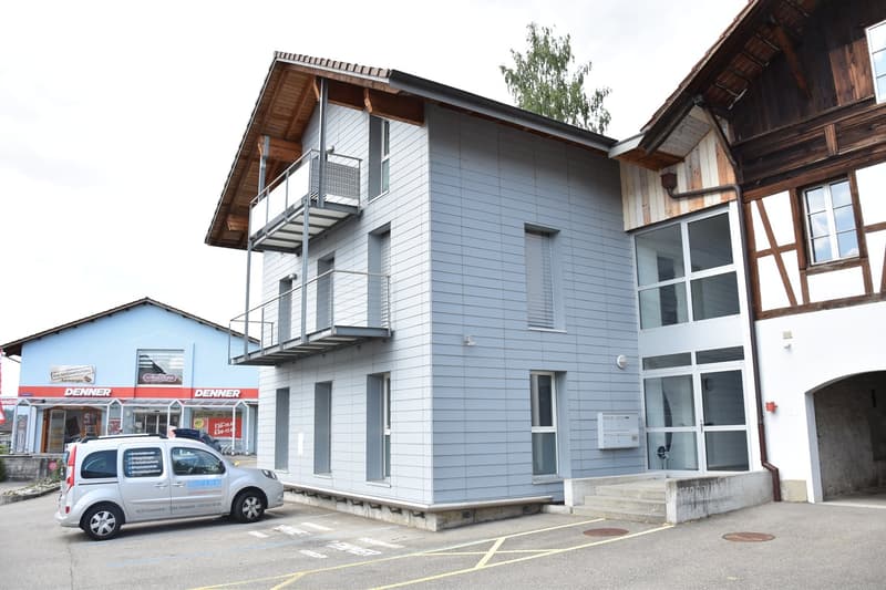 Blue residential building with wooden elements, balcony, and a parked van in front