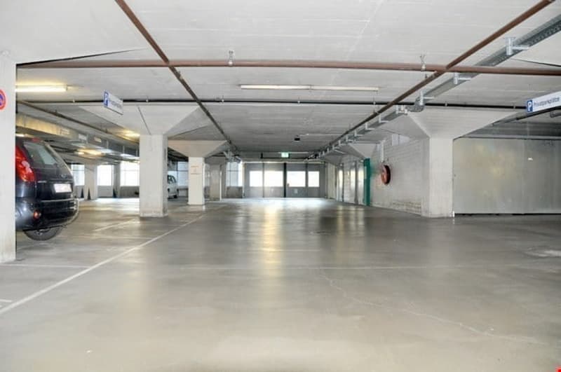 Large parking lot, concrete floor, white walls, open space, metal beams