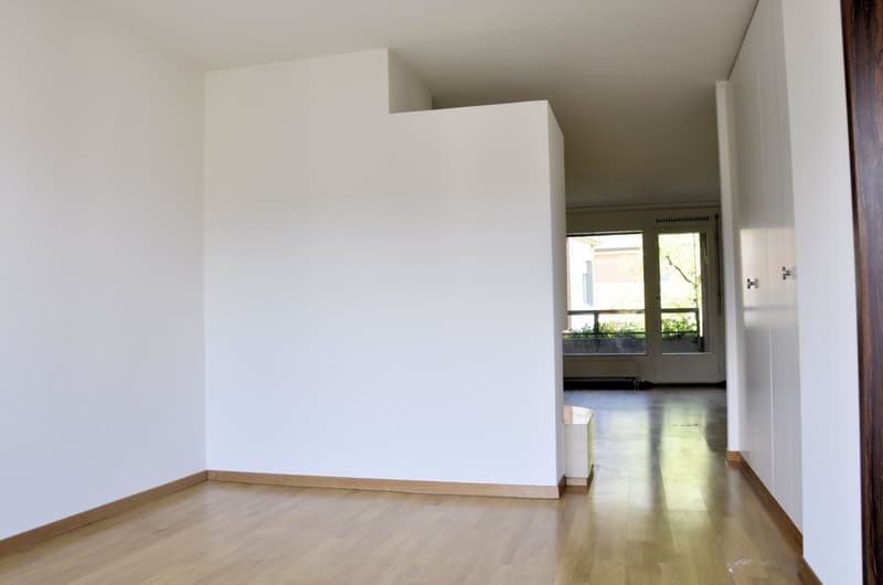 Empty room with white walls, wooden floor, and a window with a view of the outside.