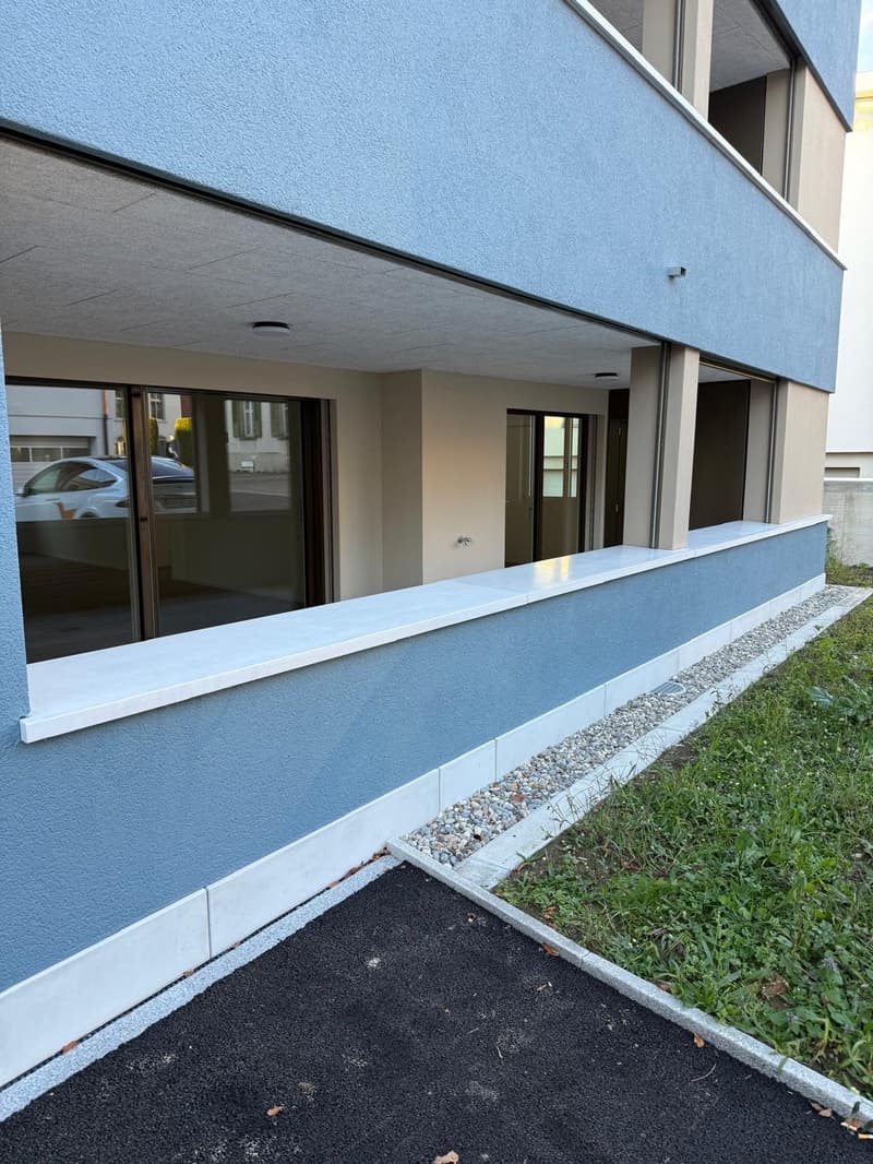 Raised ground floor blue wall, glass windows, parking area, gravel driveway