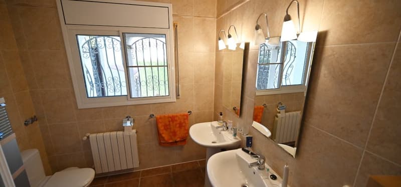 Spacious bathroom with large windows, tiled walls, two sinks, mirrors, and radiator