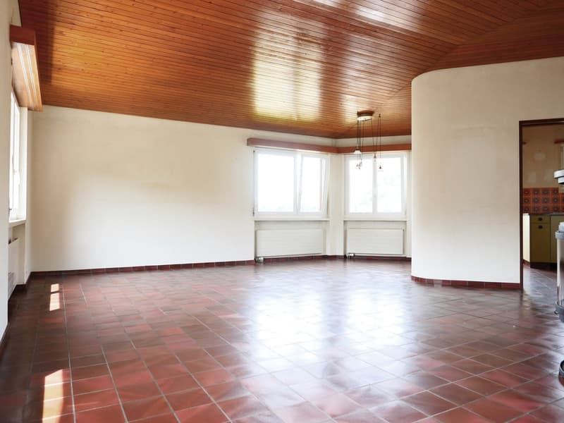 Empty room with wooden ceiling, white walls, red tiled floor, three windows, and two white radiators.
