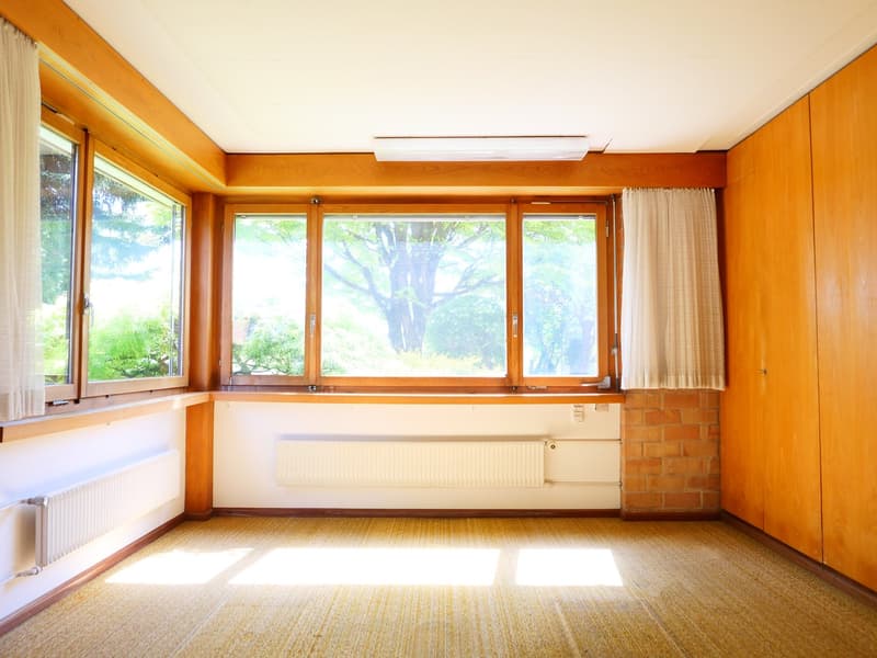 Large windows overlooking a garden, wooden paneled walls, hardwood floor, radiator, curtains