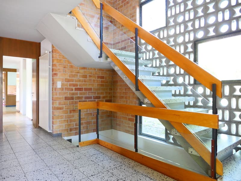 Wooden staircase with glass steps, brick walls, large windows providing natural light