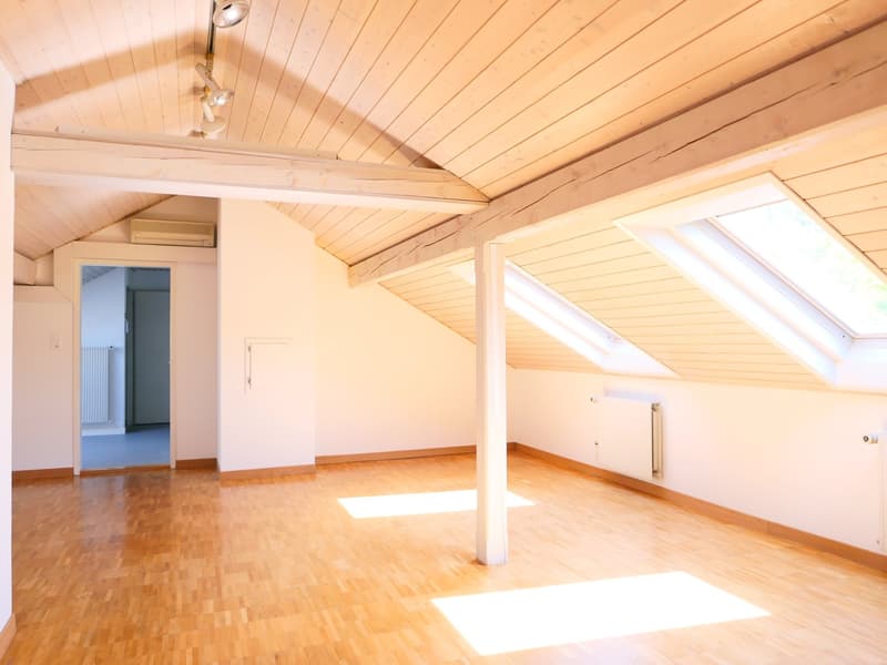 Spacious attic room with wooden paneled ceiling, hardwood flooring, and large windows providing ample natural light. The room appears to be empty and ready for potential use as a bedroom, office, or storage space.