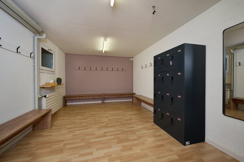 Wooden benches, coat hooks, metal lockers, pink wall, wooden floor, wooden window frame, mirror