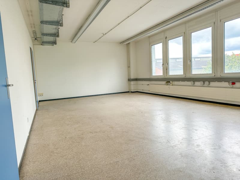Empty room with white walls, beige floor, three windows, blue door, ceiling with metal beams and lights