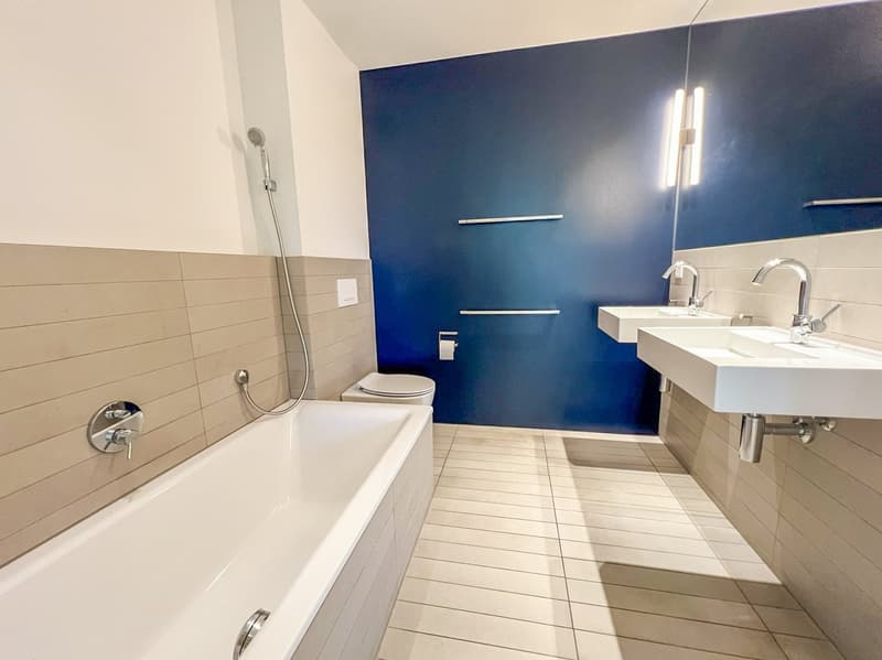 modern bathroom with bathtub, two sinks, toilet, blue wall, white tiles, shower head