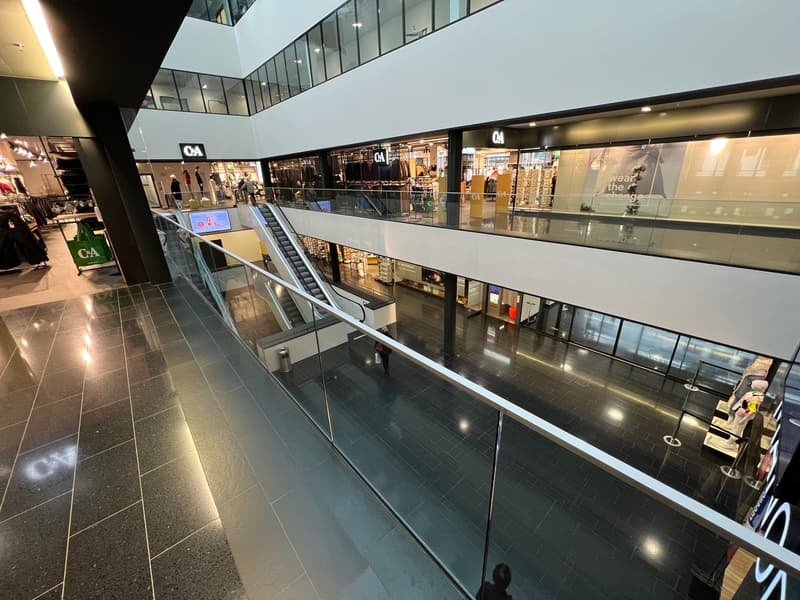Commercial space, multi-level building, glass railings, escalators, shop windows, tiled floors