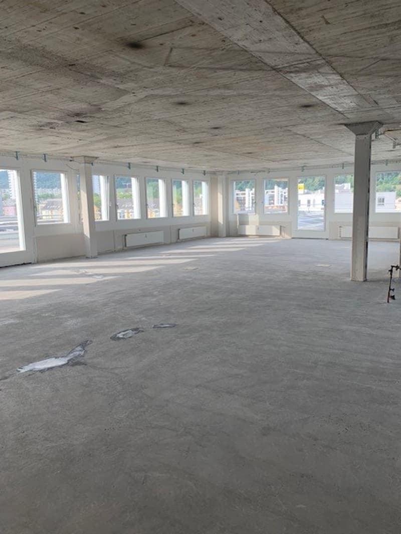 empty office space, large windows, concrete floor, exposed ceiling beams, potential for customization, city view