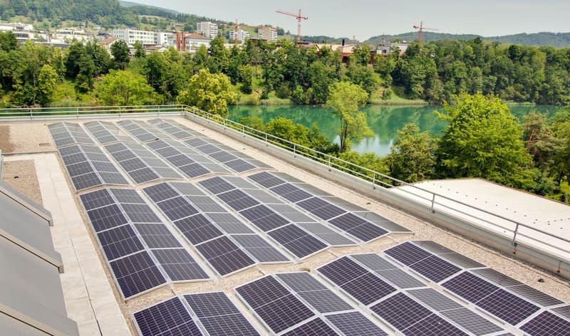 solar panels on rooftop, fence around, overlooking river and city buildings, green trees and hills in background