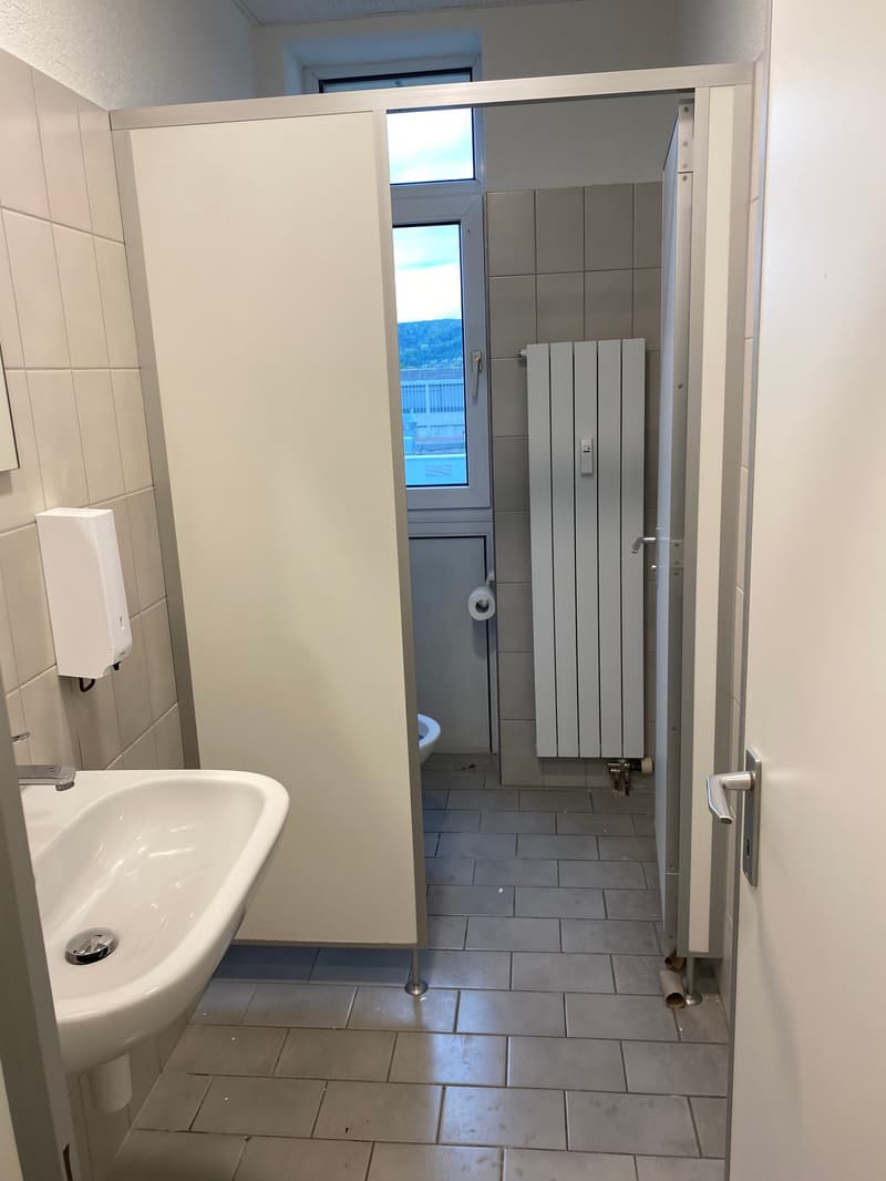 A white bathroom with tiled floor and walls, white sink, and white partitions