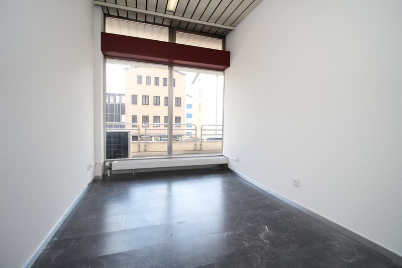 Empty room with large windows, concrete floor, and a red-colored ledge or shelf along the wall.