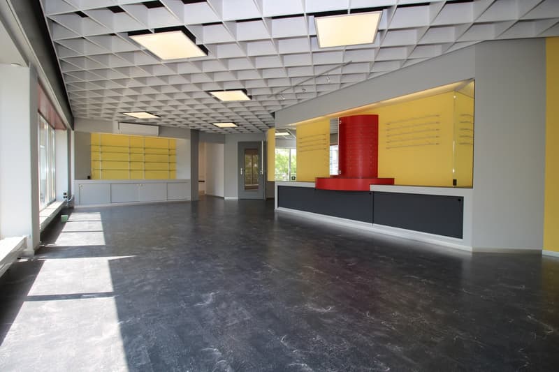 Large open office space with a grid-like ceiling, yellow and red accents on the walls, and a black and gray reception desk area.