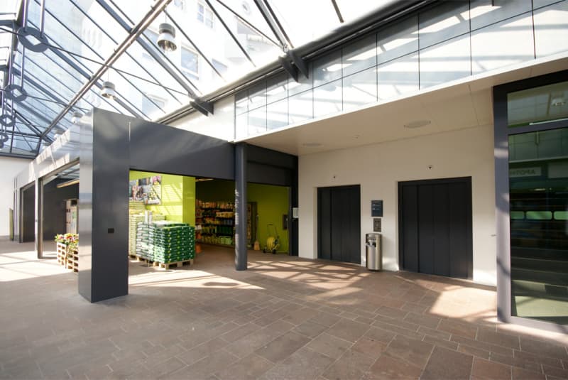 tiled floor, large glass wall, elevator, green office wall with picture, store with merchandise, and a trash bin.