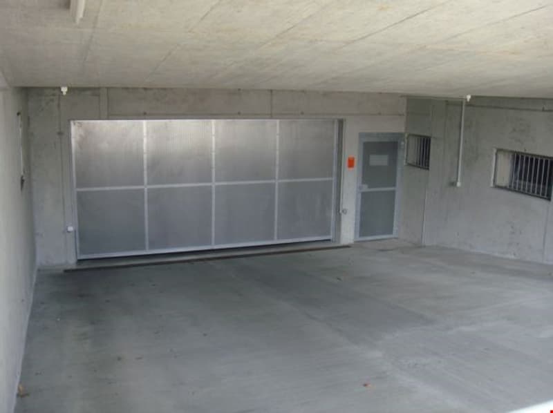 Empty concrete garage with a large roll-up door and a small door on the right side