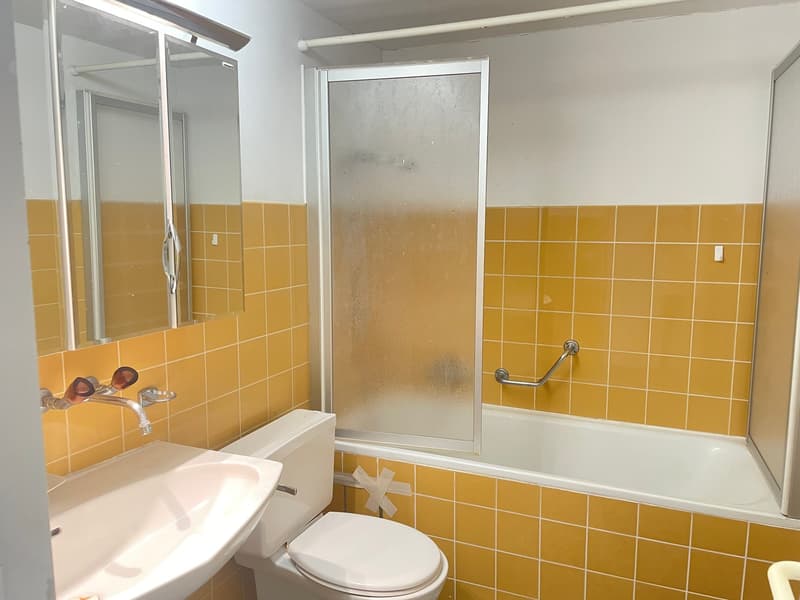 Bathroom with yellow tiles, white sink, white toilet, glass shower enclosure, bathtub, mirror, faucet