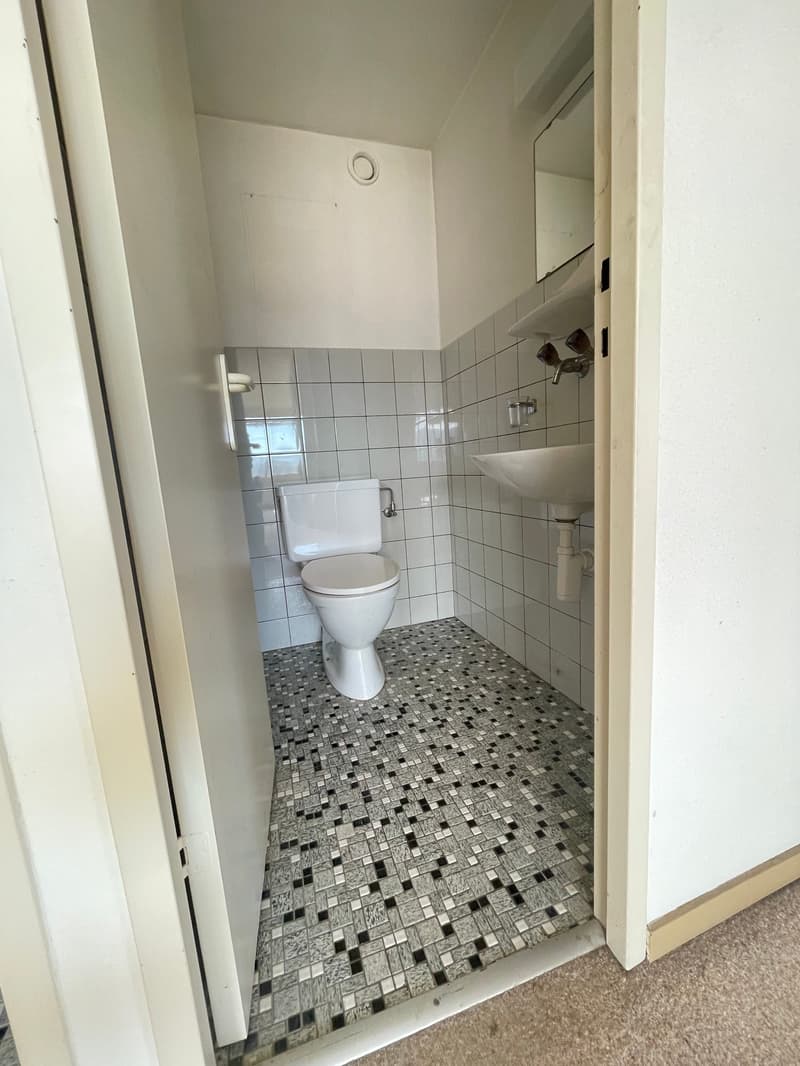 Small compact bathroom with tiled walls, white ceramic sink, toilet, and ceramic floor, white tiled walls.