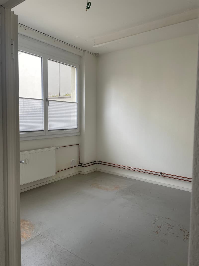 empty room, white walls, white floor, window with blinds, radiator, pipes on the wall