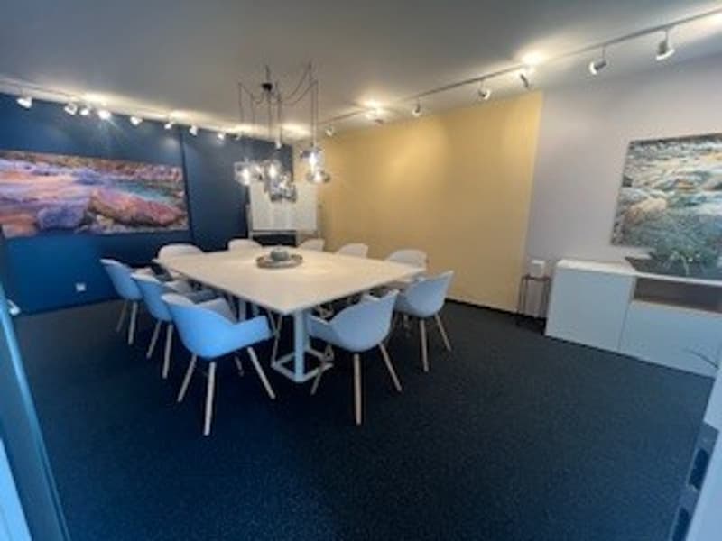 empty meeting room with a long white table, blue chairs, blue walls, yellow wall, paintings, lights