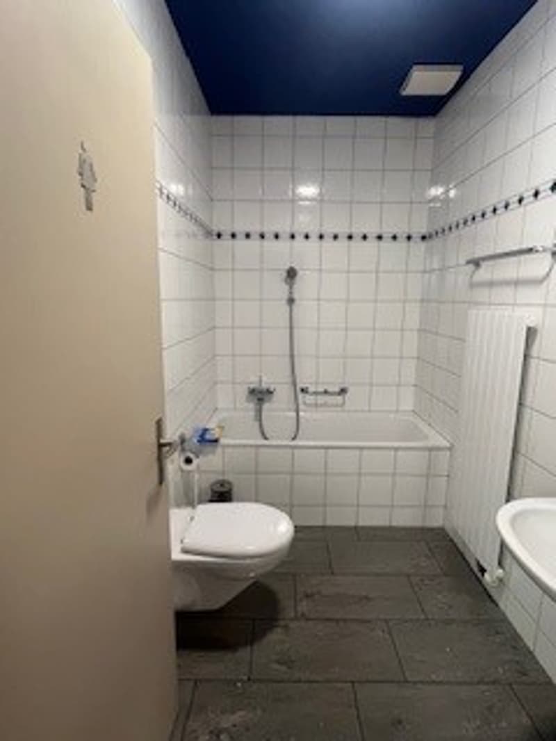 Bathroom with white tiles, bathtub, toilet, sink, shower head, radiator