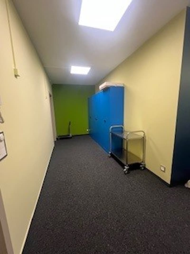Empty hallway with yellow and green walls, blue lockers, a trolley, and a ceiling light