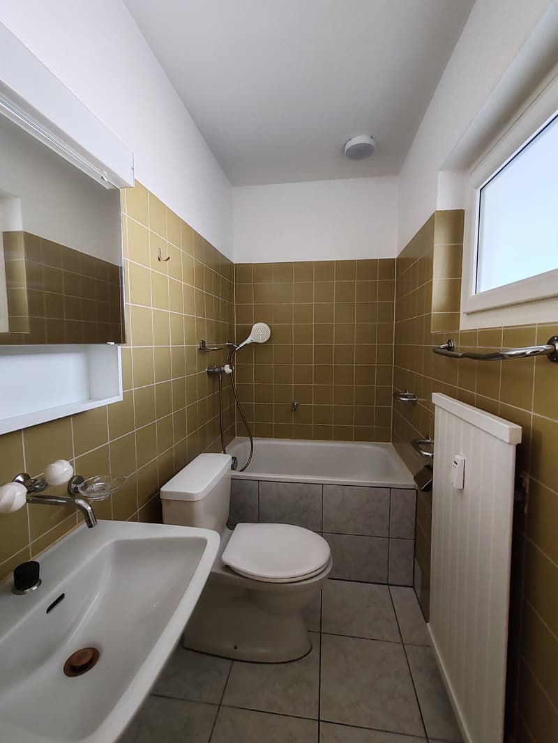 Bathroom with white toilet, white sink, white bathtub, wall-mounted mirror, tiled walls, window, and radiator