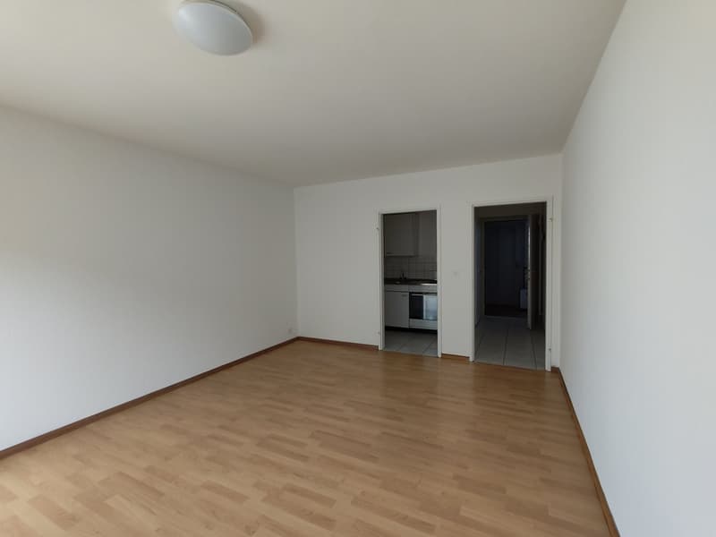 empty room, wooden floor, white walls, recessed ceiling light, doors leading to kitchen and bathroom