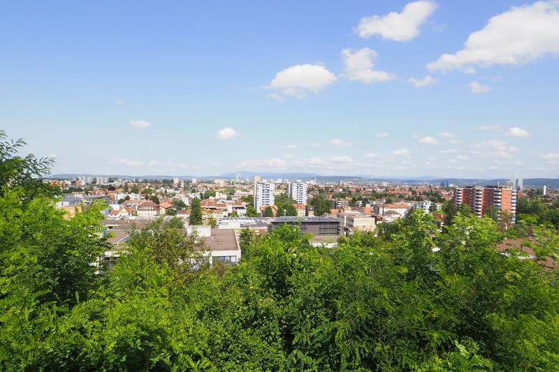 Aerial view of a city with many buildings, trees, and a clear blue sky with clouds