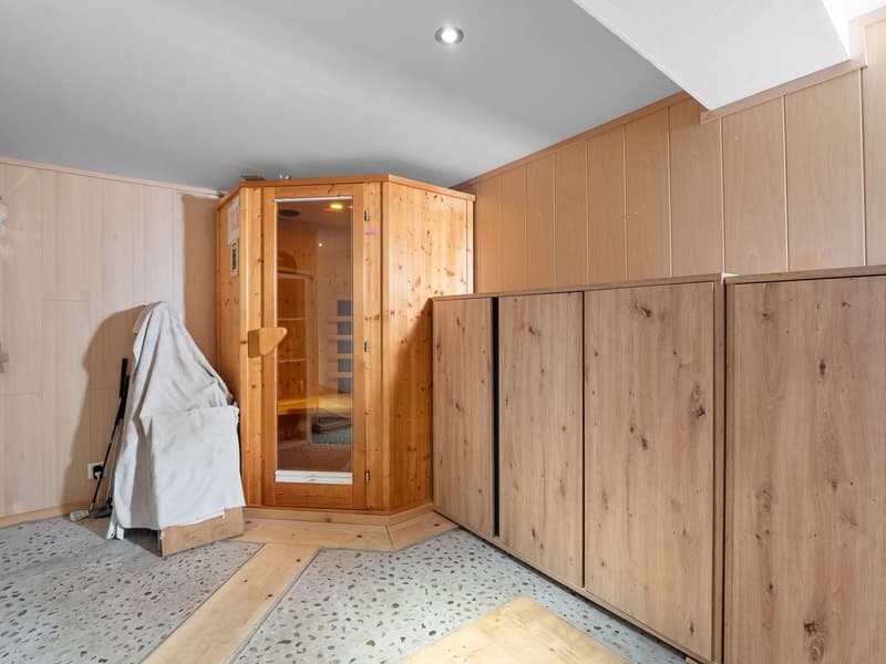 The image shows a room with wooden paneled walls and floors, a wooden sauna or steam room enclosure, and a washing machine or other laundry appliance visible in the corner.