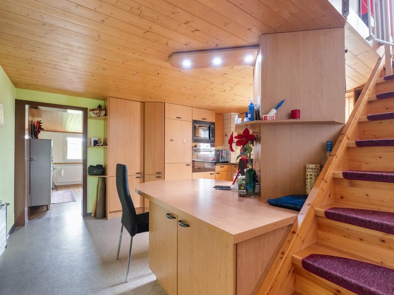 Cozy wooden kitchen with built-in cabinets, countertop, microwave, and dishwasher. Stairs leading to a loft or upper level. Warm and inviting atmosphere with wooden ceiling and walls.