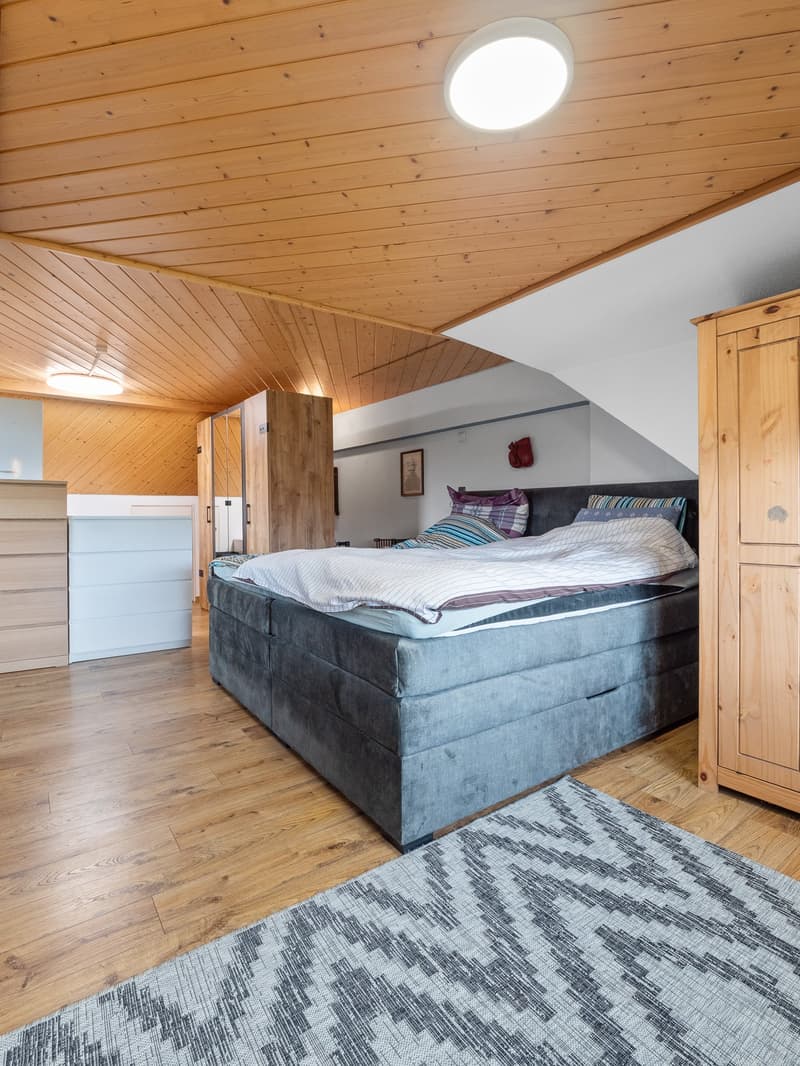 Spacious bedroom with wooden ceiling and walls, large bed, wooden furniture, and a patterned rug on the floor.
