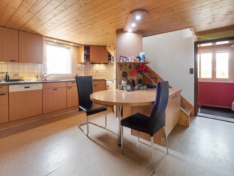 Wooden kitchen with cabinets, round dining table, black chairs, tiled floor, and a window