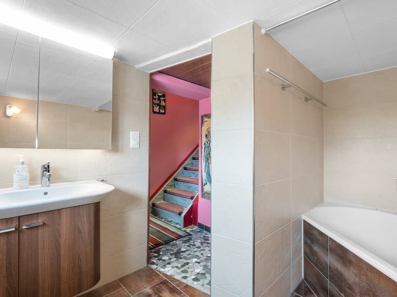 The image shows a bathroom with a vanity sink, tiled walls, and a doorway leading to a staircase with colorful steps.