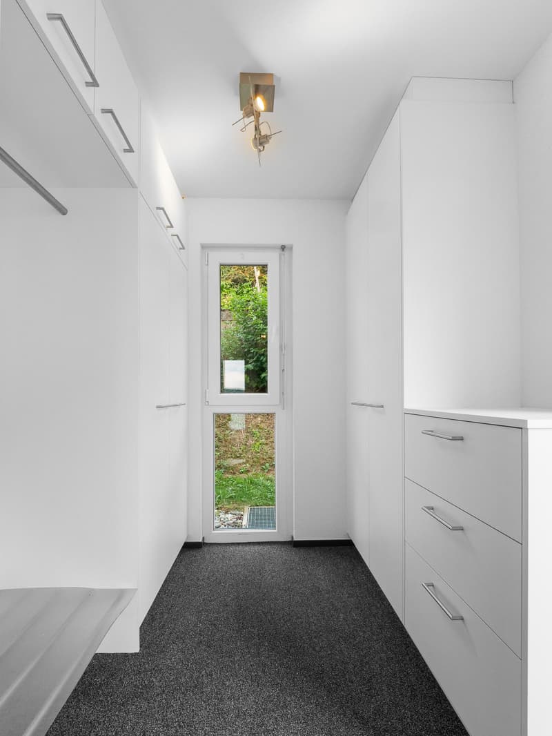 Walk-in closet with white cabinetry, dark carpet, and a glass door leading to a green outdoor area.