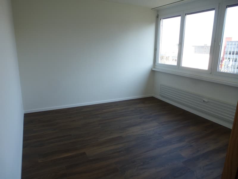 empty room with white walls, wooden floors, and large window with a view of the outside