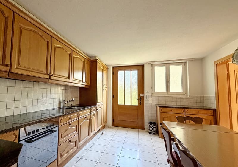 kitchen with wooden cabinets, sink, stove, white tiles, wooden dining table, window, trash bin