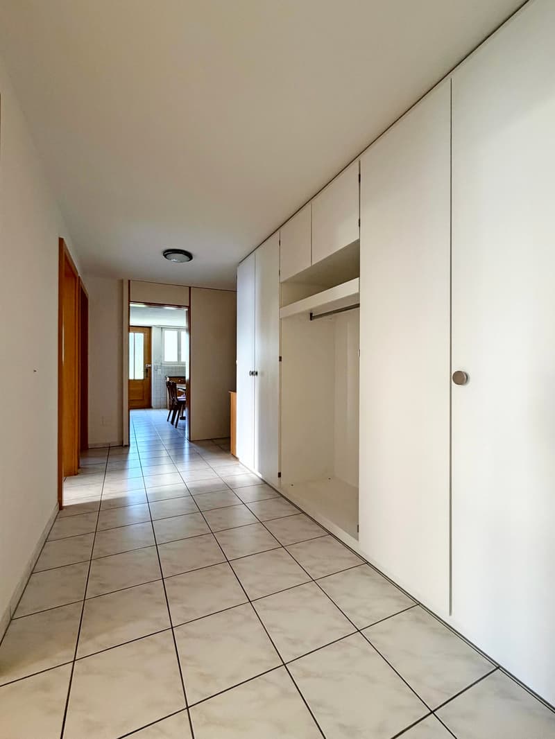 Empty hallway with tiled floor, white built-in wardrobes, open door leading to a dining room, and another open door to an adjacent room with wooden floor.