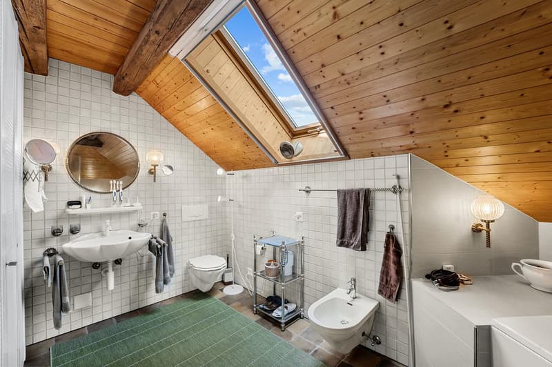 a small bathroom with a toilet, sink, mirror, and bathtub, white tiles, wooden ceiling