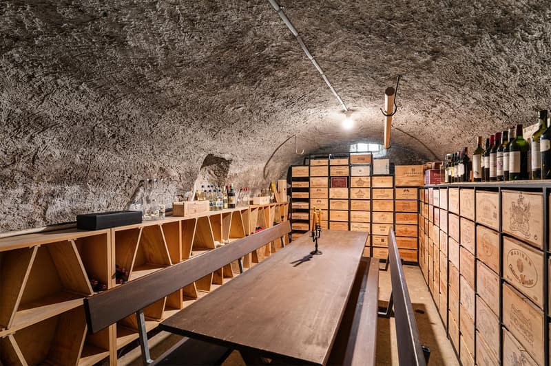 cellar with wooden shelves, wine bottles, dining table, benches, and warm lighting