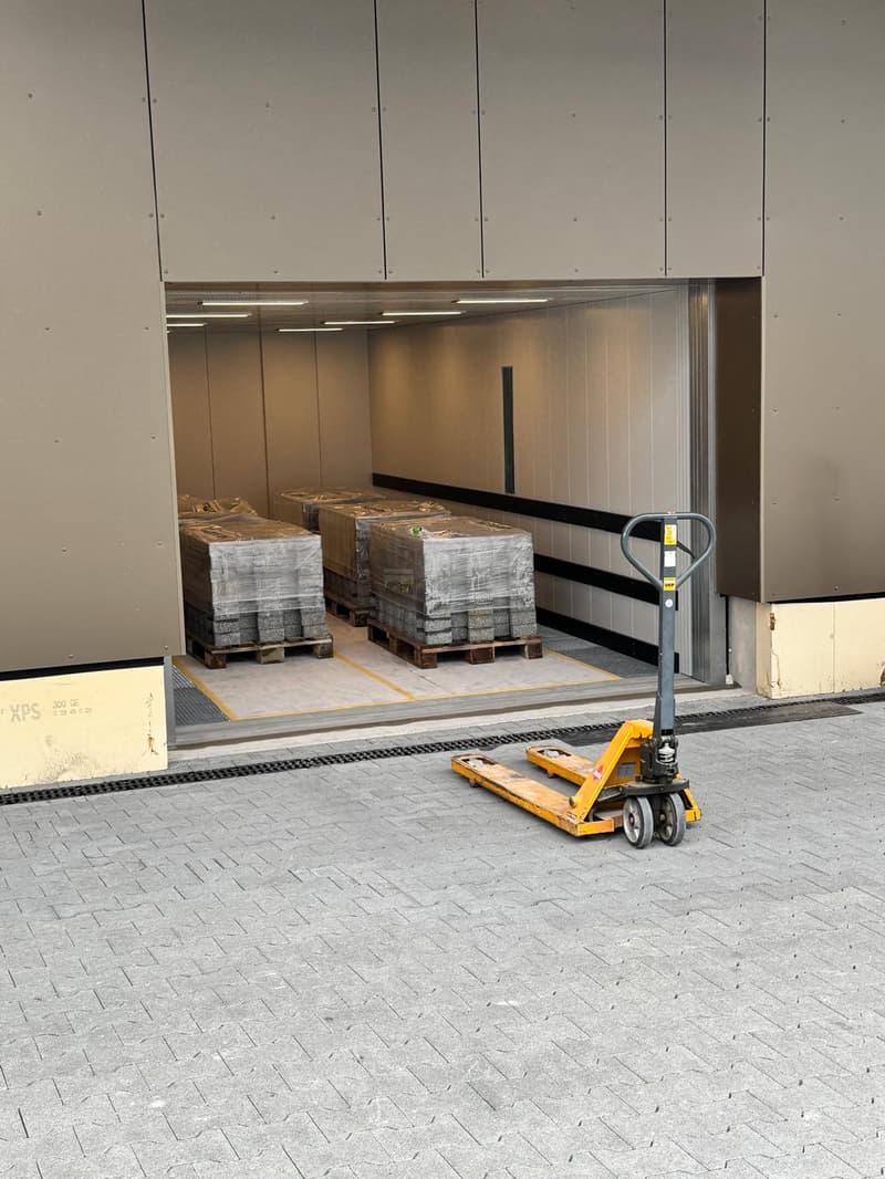 Industrial building with a large open door, pallet jack in front, several pallets inside