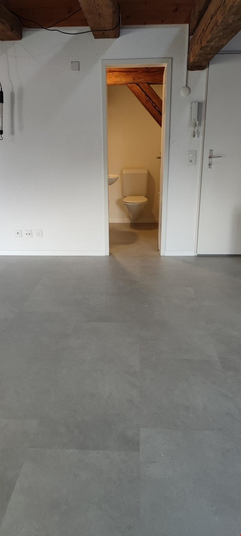 Bathroom with white walls, wooden beams, and a toilet visible through the open doorway
